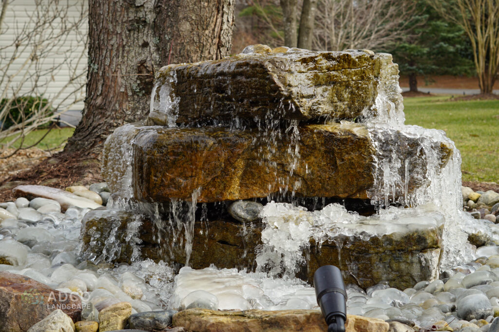 A natural boulder water feature with ice forming around the base.