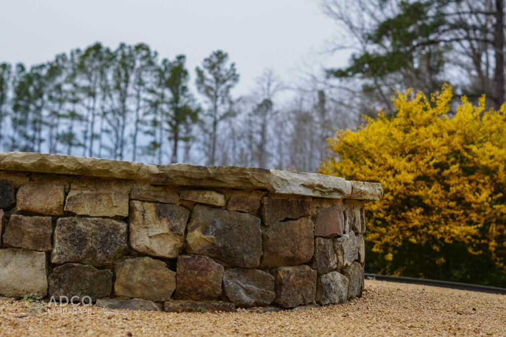 A stone fire pit with shrubs and trees in the background.