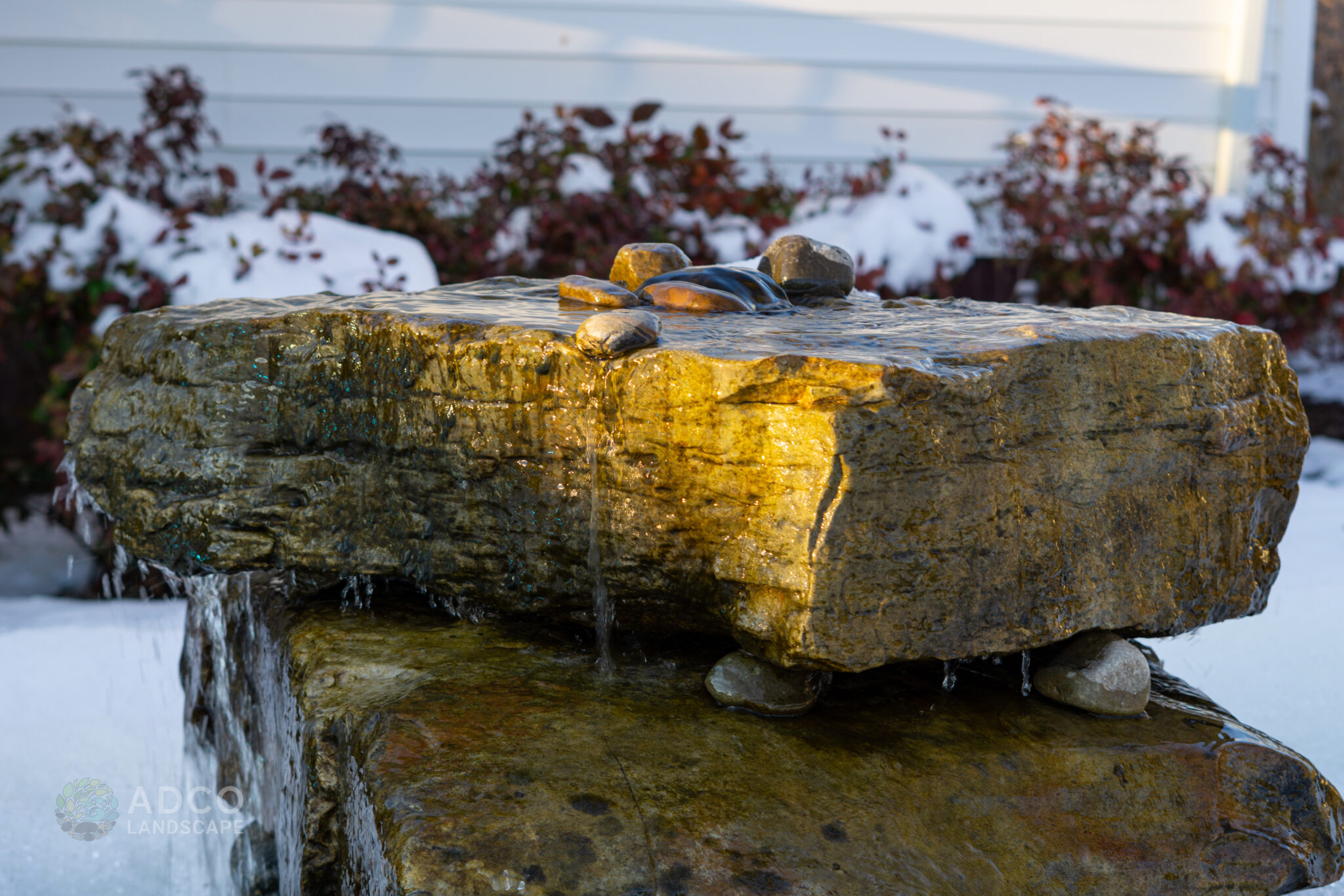 A Custom Natural Boulder Water Feature with red shrubs in the background in the snow.