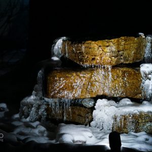 A Custom Natural Boulder Water Feature with Outdoor Lights, Ice Around it at night.